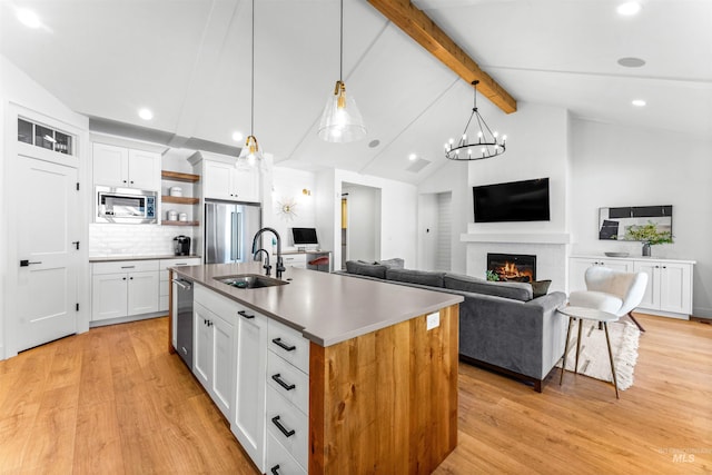 kitchen with vaulted ceiling with beams, a center island with sink, white cabinets, and appliances with stainless steel finishes