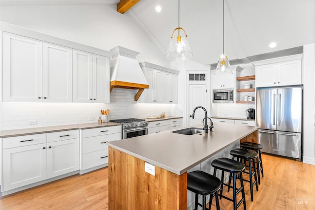 kitchen featuring high quality appliances, a kitchen island with sink, lofted ceiling with beams, sink, and custom range hood