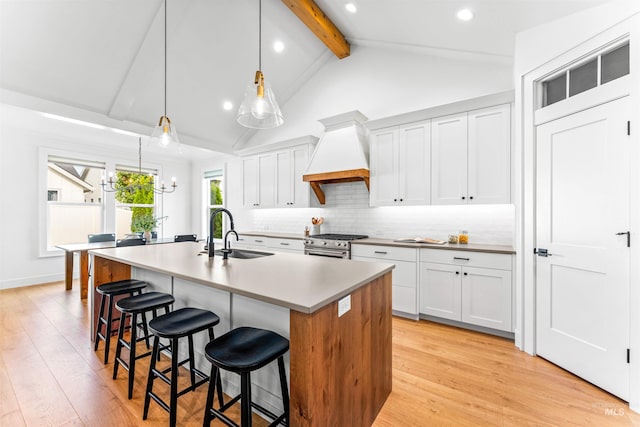 kitchen with a center island with sink, vaulted ceiling with beams, white cabinetry, and premium range hood