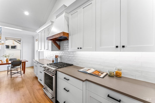 kitchen featuring custom exhaust hood, stainless steel range, vaulted ceiling, light hardwood / wood-style floors, and white cabinetry