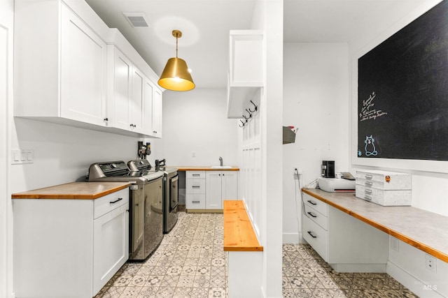 kitchen with washing machine and clothes dryer, sink, butcher block countertops, pendant lighting, and white cabinets