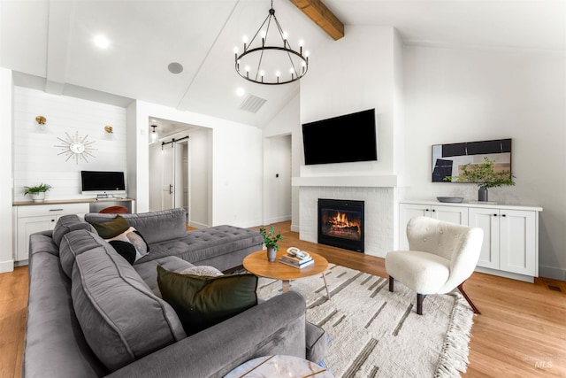 living room featuring light wood-type flooring, a fireplace, a barn door, an inviting chandelier, and beamed ceiling