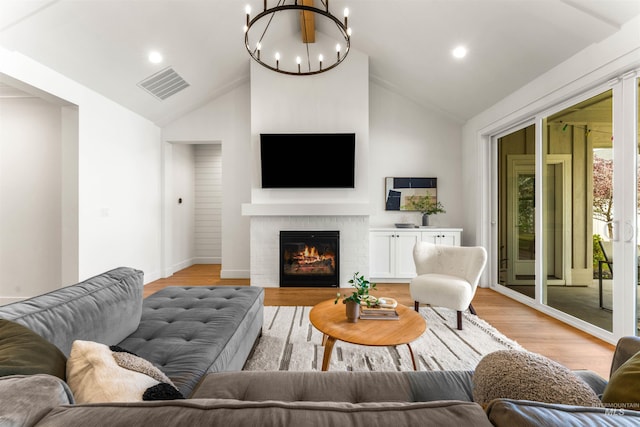 living room featuring a fireplace, an inviting chandelier, lofted ceiling, and light hardwood / wood-style flooring