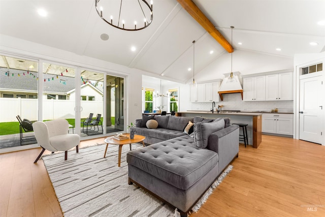 living room featuring beam ceiling, sink, high vaulted ceiling, a chandelier, and light wood-type flooring