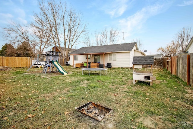 rear view of house featuring a trampoline, a fenced backyard, a lawn, and a playground