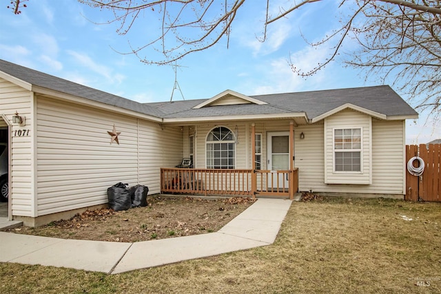 ranch-style home with a porch, fence, a front yard, and a shingled roof