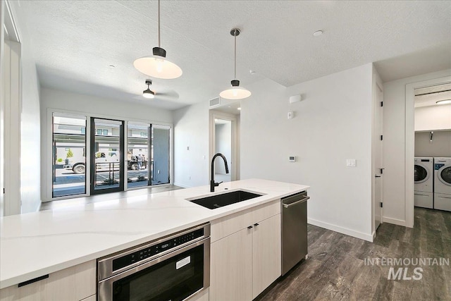 kitchen featuring washer and clothes dryer, sink, hanging light fixtures, a textured ceiling, and light stone counters