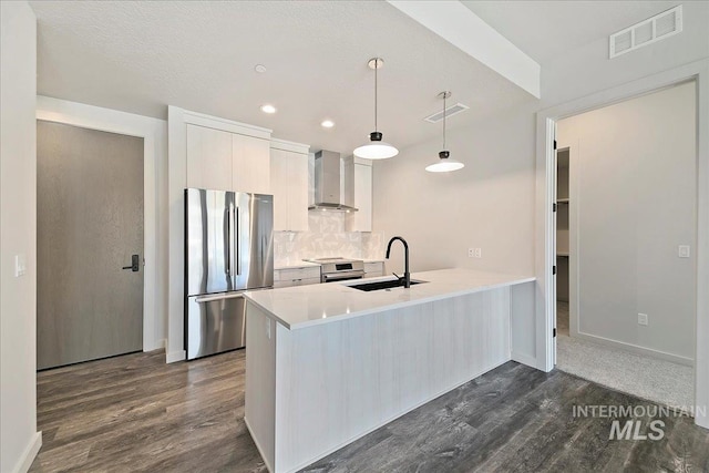 kitchen with sink, wall chimney exhaust hood, pendant lighting, white cabinets, and appliances with stainless steel finishes