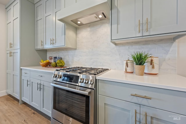 kitchen featuring light hardwood / wood-style flooring, premium range hood, gray cabinetry, stainless steel range with gas stovetop, and tasteful backsplash