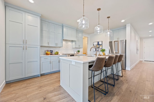 kitchen featuring sink, a breakfast bar area, stainless steel refrigerator, pendant lighting, and a kitchen island with sink