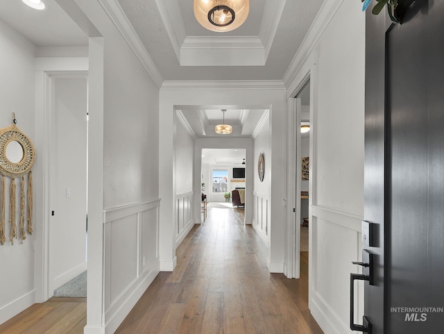 corridor with crown molding, a raised ceiling, a decorative wall, and wood-type flooring