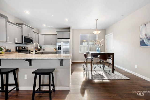 kitchen featuring sink, gray cabinets, stainless steel appliances, tasteful backsplash, and light stone countertops