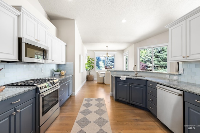 12258 Whitechapel Way, Nampa, ID 83686 - kitchen with appliances with stainless steel finishes, a sink, white cabinets, light wood-style flooring, and backsplash