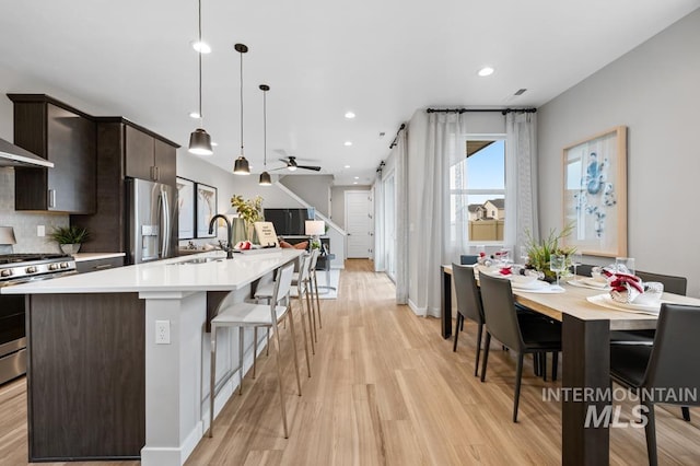 kitchen featuring light wood finished floors, a sink, stainless steel appliances, light countertops, and backsplash