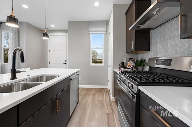 kitchen with light countertops, wall chimney range hood, appliances with stainless steel finishes, and a sink