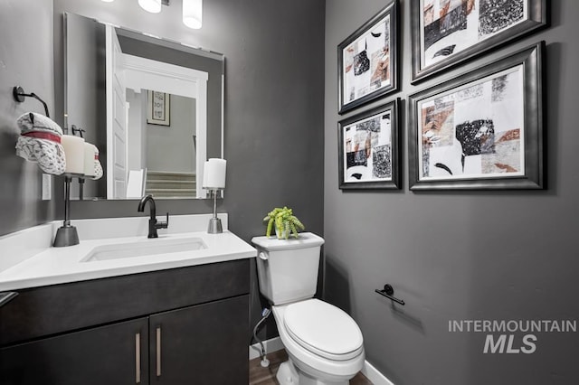 half bath featuring baseboards, toilet, and vanity