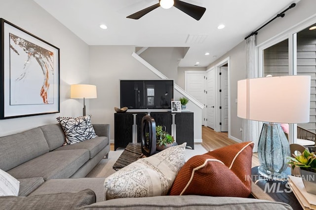 living area with light wood-type flooring, recessed lighting, stairway, baseboards, and ceiling fan