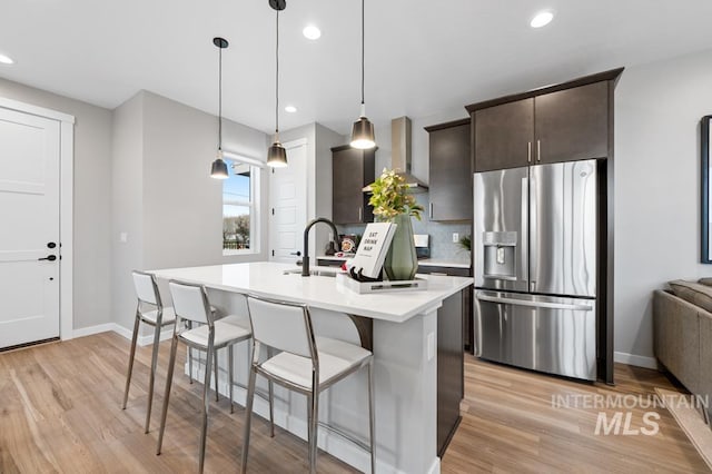 kitchen featuring a kitchen island with sink, stainless steel fridge, a breakfast bar area, light countertops, and dark brown cabinets