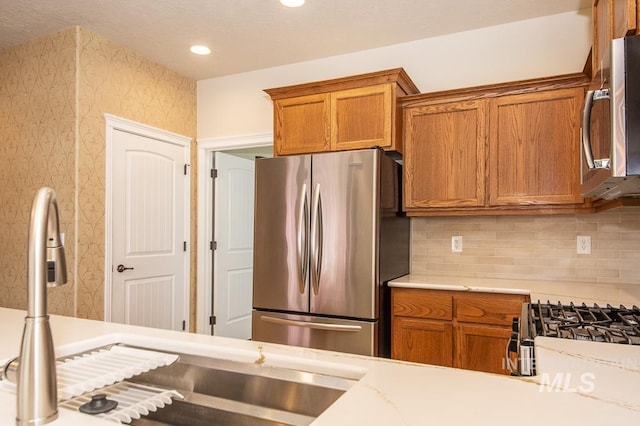 325 S Whisperwood Way, Boise, ID 83709 - kitchen featuring wallpapered walls, tasteful backsplash, brown cabinets, and stainless steel appliances