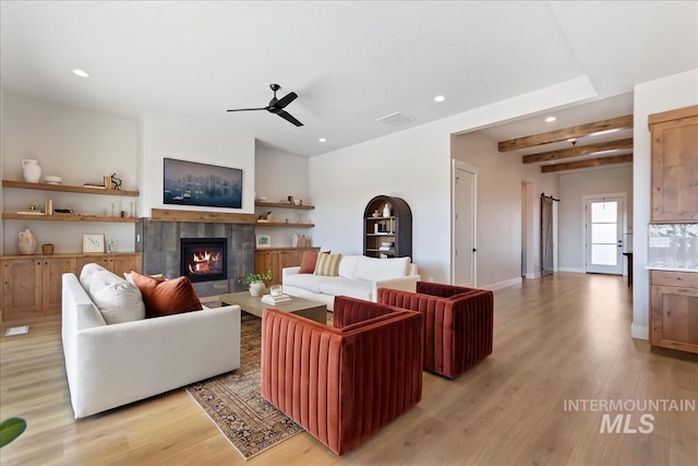 living room with a tiled fireplace, beam ceiling, ceiling fan, and light wood-type flooring