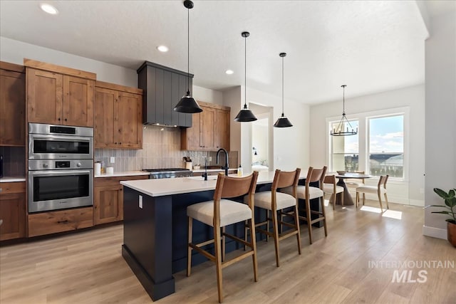 kitchen featuring a breakfast bar area, decorative light fixtures, an island with sink, stainless steel double oven, and decorative backsplash