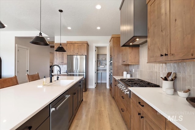 kitchen with pendant lighting, sink, stainless steel appliances, decorative backsplash, and light wood-type flooring