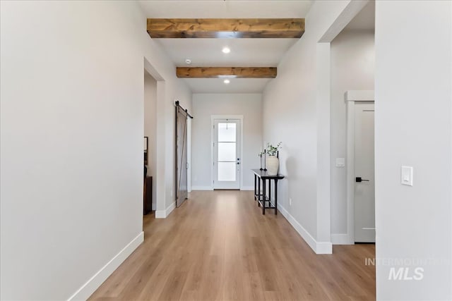 hallway with a barn door, light hardwood / wood-style floors, and beam ceiling