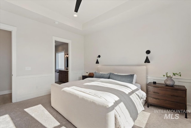 carpeted bedroom featuring ceiling fan, connected bathroom, and a tray ceiling