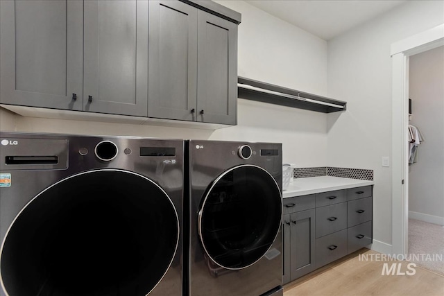 laundry room featuring washer and clothes dryer, cabinets, and light wood-type flooring