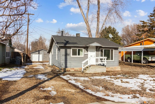 view of front facade with a detached garage, driveway, a chimney, and an outdoor structure