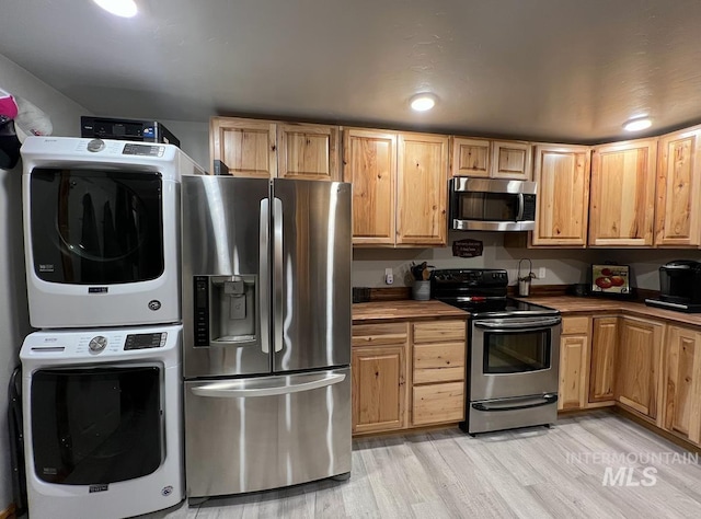 kitchen with stainless steel appliances, stacked washer / drying machine, and light wood-type flooring