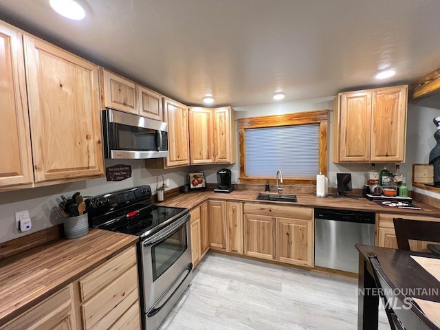 kitchen featuring sink, light brown cabinets, butcher block countertops, appliances with stainless steel finishes, and light wood-type flooring