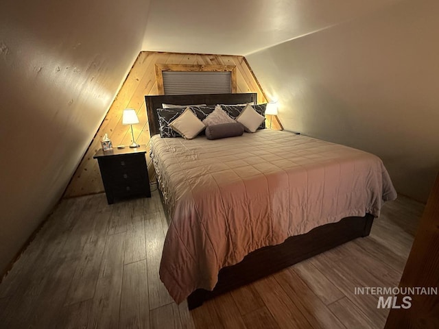 bedroom with wooden walls, hardwood / wood-style flooring, and lofted ceiling