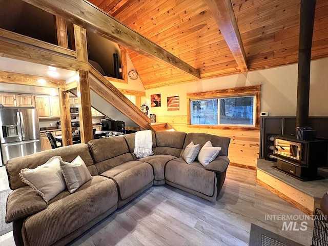 living room featuring a wood stove, wooden walls, vaulted ceiling with beams, light hardwood / wood-style floors, and wood ceiling