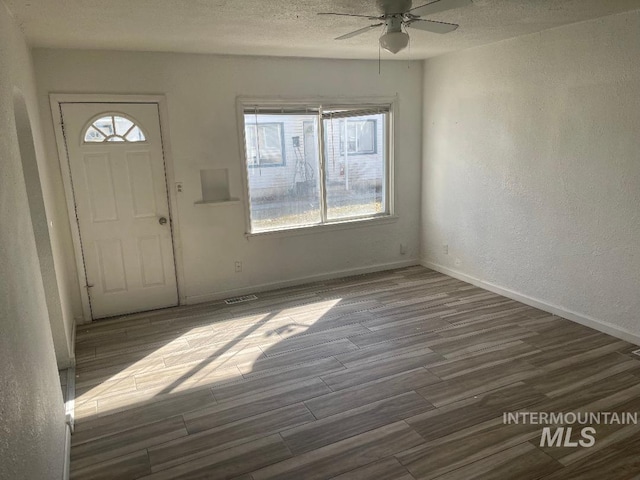 entryway featuring baseboards, visible vents, wood finished floors, ceiling fan, and a textured wall