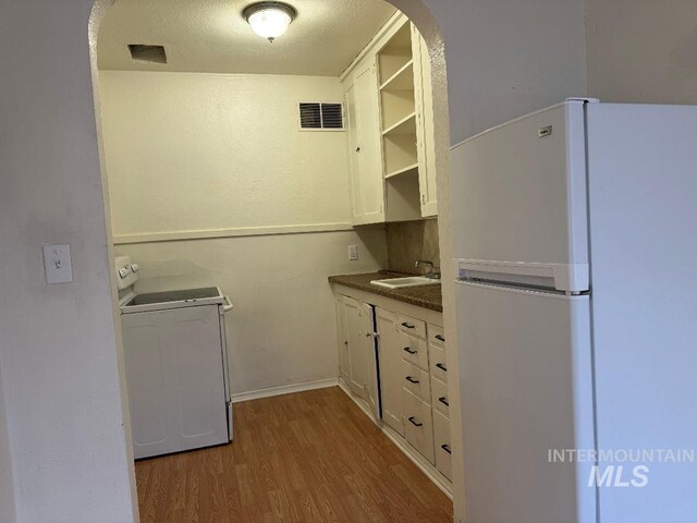 kitchen with open shelves, wood finished floors, visible vents, freestanding refrigerator, and washer / clothes dryer
