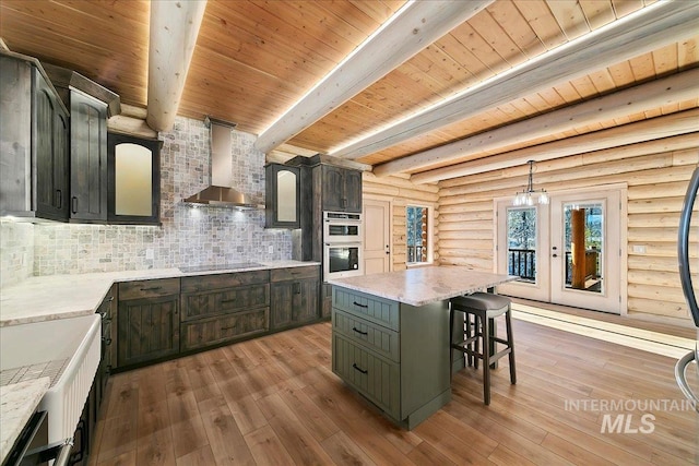 kitchen with wall chimney exhaust hood, a kitchen island, light hardwood / wood-style floors, and log walls