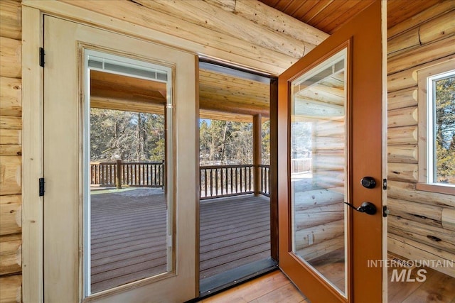 doorway to outside with light hardwood / wood-style floors, wood ceiling, rustic walls, and a wealth of natural light