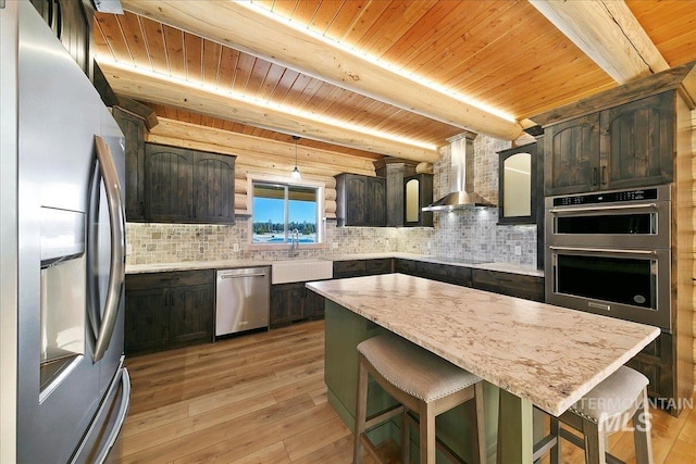 kitchen featuring light wood-type flooring, appliances with stainless steel finishes, a center island, and wall chimney range hood