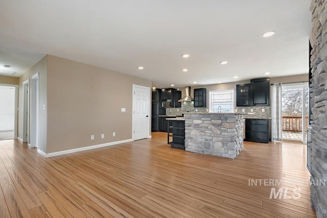 kitchen with light stone countertops, backsplash, wall chimney range hood, light hardwood / wood-style flooring, and a center island