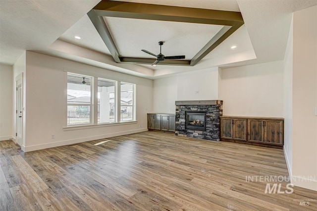 unfurnished living room with a stone fireplace, a tray ceiling, and wood finished floors