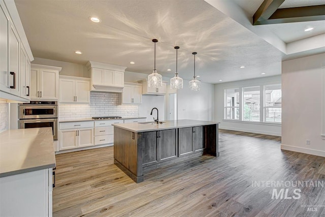 kitchen with a sink, stainless steel appliances, tasteful backsplash, and light wood finished floors