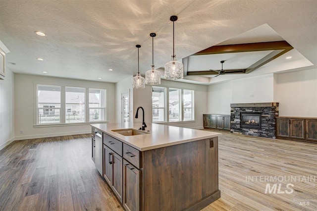 kitchen with light wood finished floors, open floor plan, a stone fireplace, plenty of natural light, and a sink