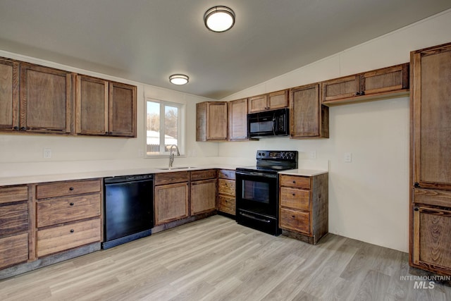 kitchen with black appliances, light hardwood / wood-style flooring, sink, and vaulted ceiling