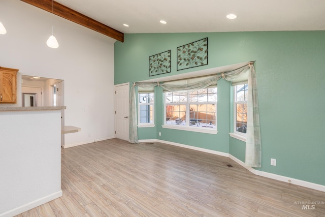 unfurnished living room featuring beam ceiling, high vaulted ceiling, a wealth of natural light, and light hardwood / wood-style flooring