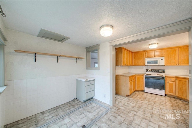 kitchen with a textured ceiling, tile walls, and white appliances