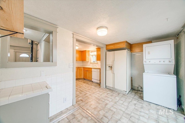 kitchen with a textured ceiling, white appliances, tile countertops, and stacked washer / drying machine