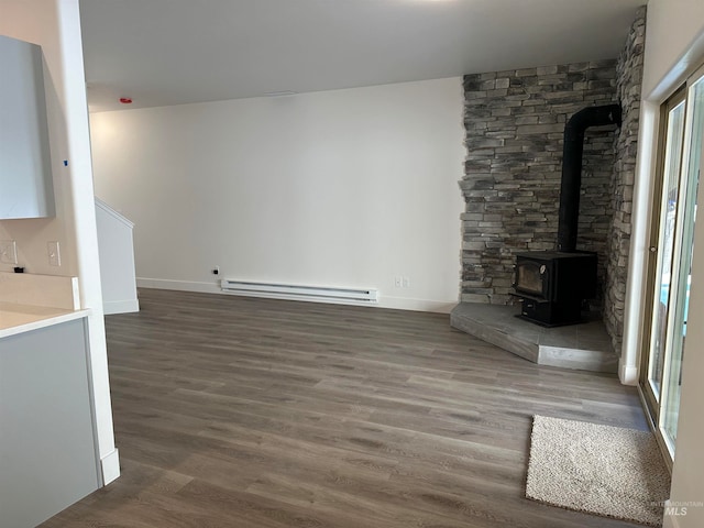 unfurnished living room featuring a baseboard heating unit, a wood stove, dark wood finished floors, and baseboards