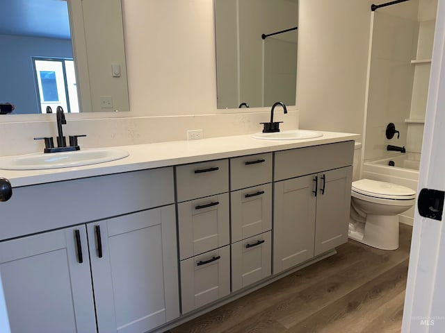 bathroom with double vanity, tub / shower combination, a sink, and wood finished floors