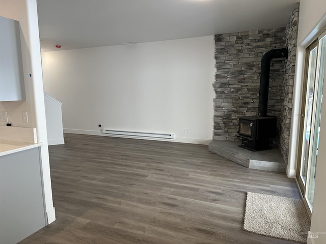 unfurnished living room featuring dark wood-type flooring, a wood stove, baseboards, and baseboard heating